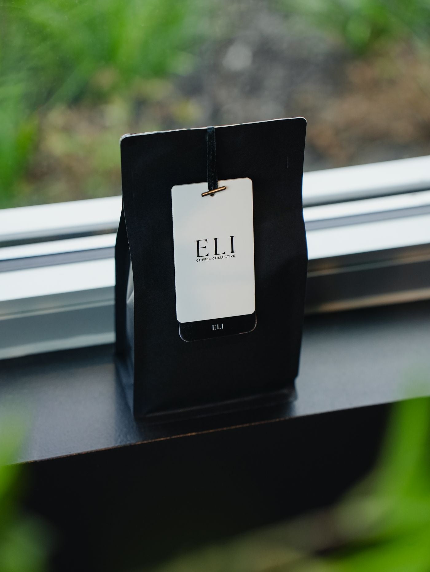A black bag of Eli coffee with a white Eli Coffee Collective tag, on a windowsill